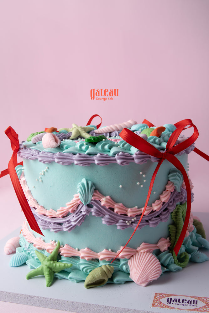 Custom mermaid theme cake decorated with pastel colors, seashells, and ribbons from Gateau Gourmet Cafe