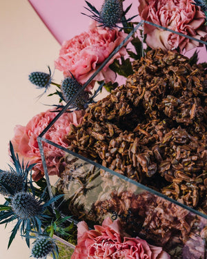 Artisan nutty chocolate clusters displayed in a glass container surrounded by pink and blue flowers