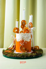 Artisan orange summer celebration cake by Gateau Gourmet Cafe decorated with dried orange slices, white candles, and floral accents