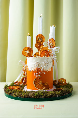 Artisan orange summer celebration cake by Gateau Gourmet Cafe decorated with dried orange slices, white candles, and floral accents