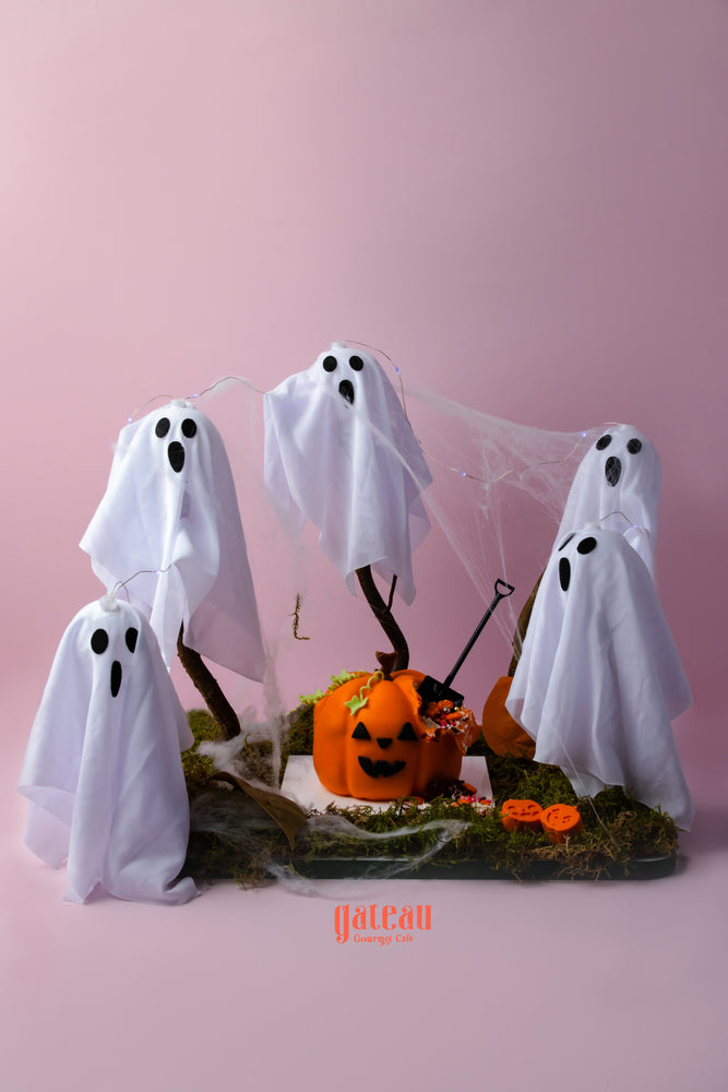 A festive display featuring a baby pumpkin cake with spooky decoration and ghostly figures around it