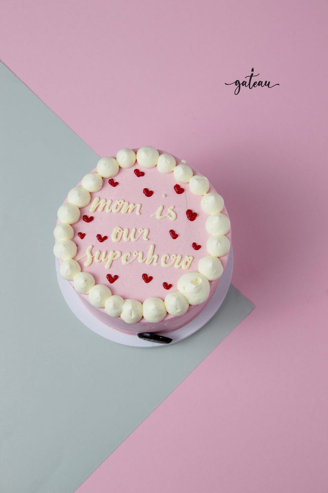 Pink cake with white frosting and red hearts saying mom is our superhero best cakes for mom by Gateau Gourmet Cafe