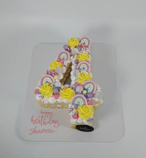 Gateau Gourmet Cafe birthday number cake decorated with yellow frosting and pastel rainbow toppers