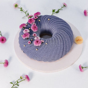 Bluish-purple mousse cake with textured swirl design and pink flower decorations by Gateau Gourmet Cafe