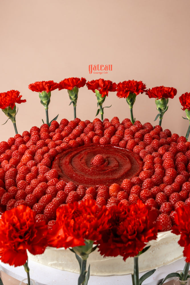 Overloaded raspberry cake topped with fresh raspberries and red flowers for a stunning dessert display