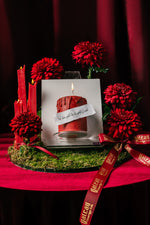 Mini candle canvas cake by Gateau Gourmet Cafe with red icing, surrounded by red flowers and candles on a green moss base