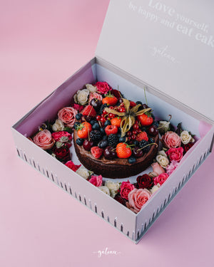 Chocolate fudge with mixed berries topped cake in gift box surrounded by pink and red roses