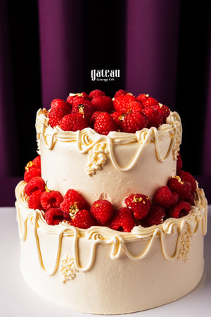 Two-tier custom birthday cake with berries decorated with white frosting and red raspberries from Gateau Gourmet Cafe