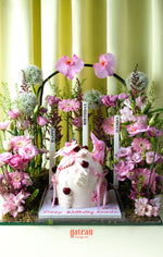 Custom cake with floral arrangement featuring pink flowers and cherries on white frosting by Gateau Gourmet Cafe