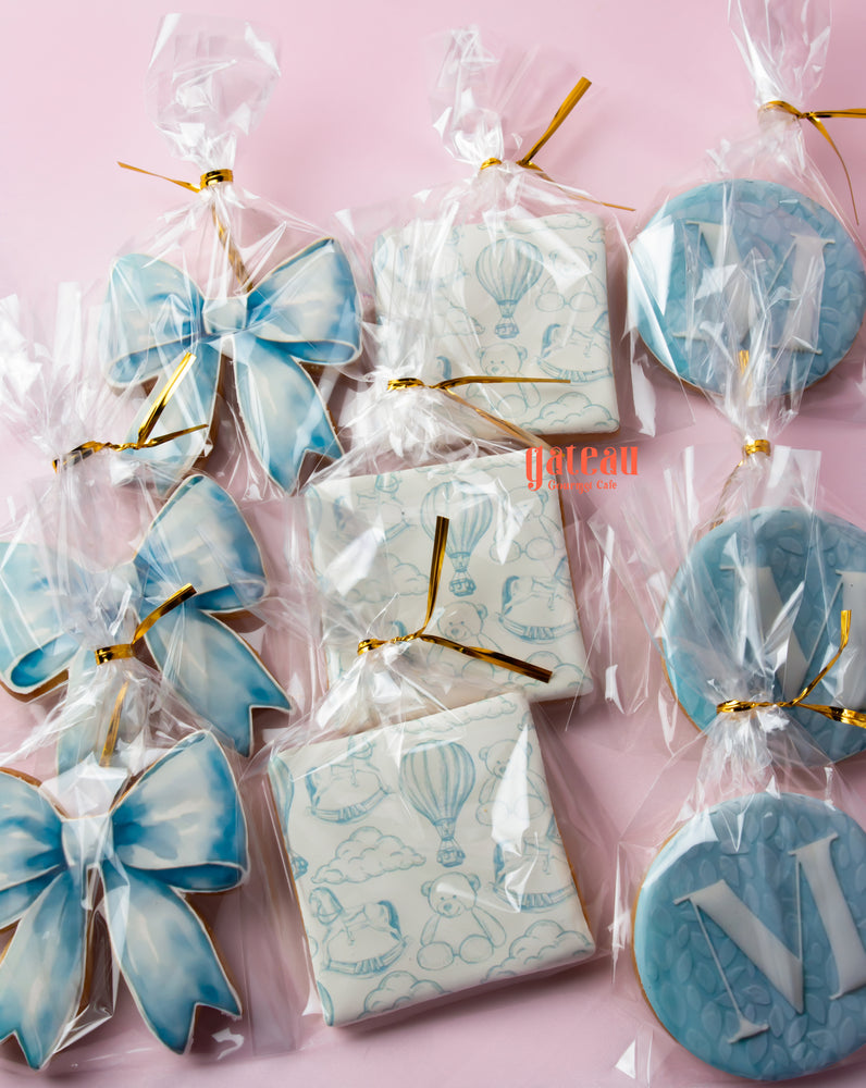 Custom decorated cookies online featuring blue bows and designs in clear packaging from Gateau Gourmet Cafe
