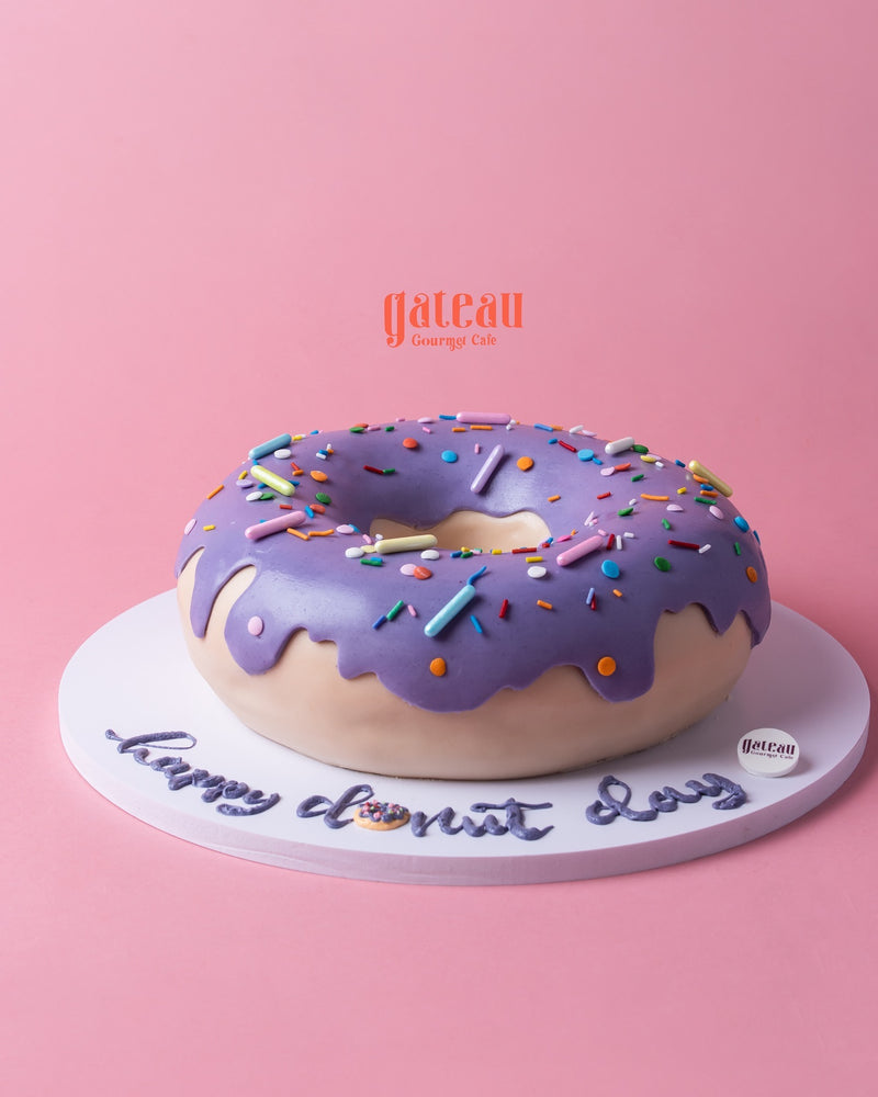 Gateau Gourmet Cafe custom donut-shaped cake with purple frosting and colorful sprinkles on a white base