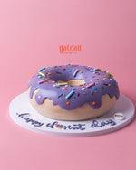 Gateau Gourmet Cafe custom donut-shaped cake with purple frosting and colorful sprinkles on a white base