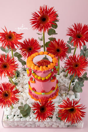Custom floral cake design by Gateau Gourmet Cafe featuring vibrant pink and orange icing with surrounding red flowers