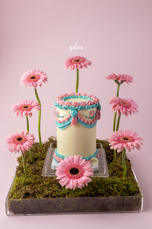 Elegant custom floral cake decorated with pink and blue icing and surrounded by pink flowers on moss base