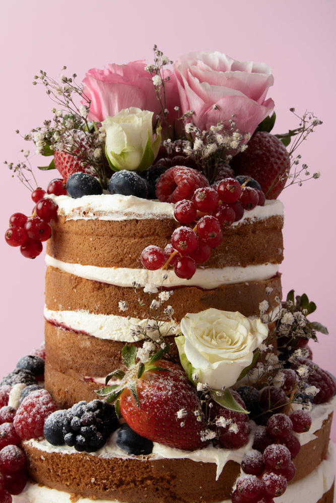 Custom naked cake with fresh fruit featuring strawberries, blueberries, and roses