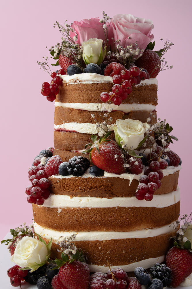 Custom naked cake with fresh fruit featuring berries and roses from Gateau Gourmet Cafe
