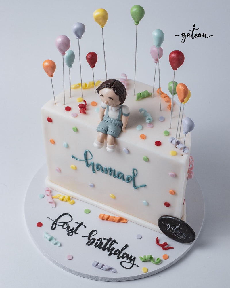Gateau Gourmet Cafe custom pastel theme cake with a sitting child figurine and colorful balloon decorations