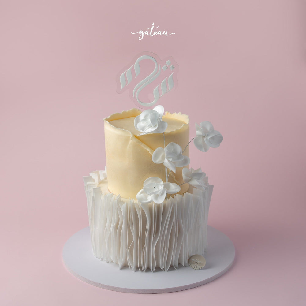 Elegant two-tier custom wedding cake with white floral accents and a custom wedding cake topper by Gateau Gourmet Cafe