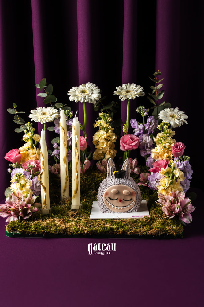 Customized graduation Labubu cake surrounded by flowers and decorative candles at Gateau Gourmet Cafe