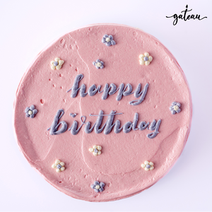 Pink birthday cake for girls decorated with purple and white flowers and happy birthday text