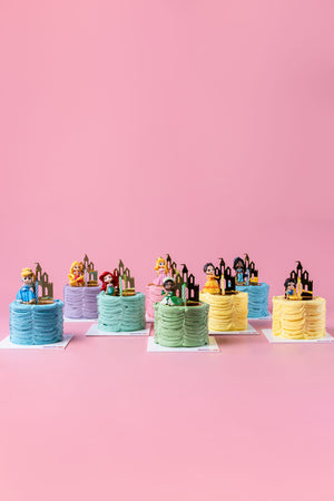 Gateau Gourmet Cafe Disney Princess Cake Design assortment with colorful frosting and princess toppers on pink background