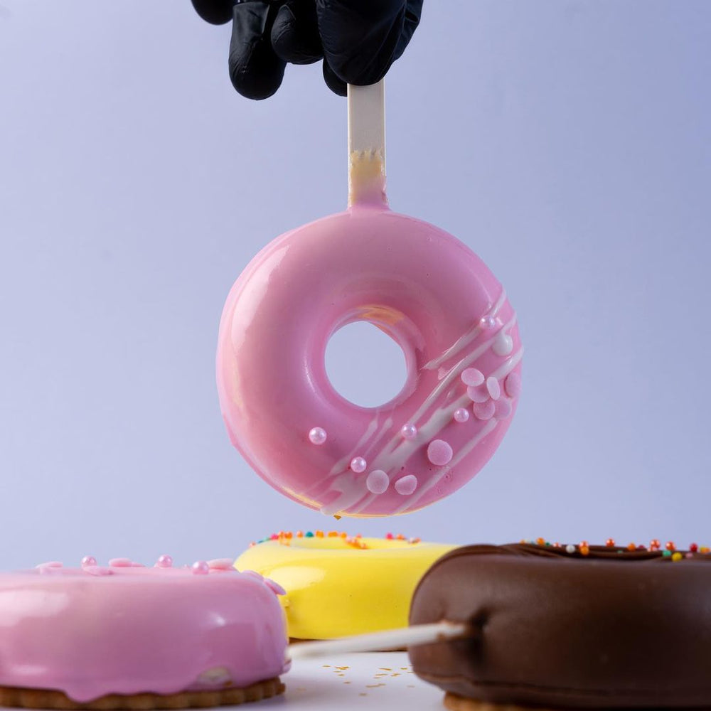 Gateau Gourmet Cafe pink donut mousse sticks with decorative icing and sprinkles held by gloved hand