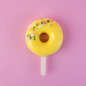 Yellow glazed donut mousse sticks with colorful sprinkles on a white stick against pink background