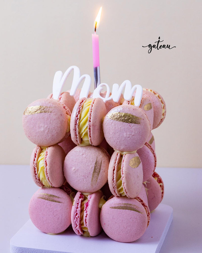 Pink fancy macaroon desserts stacked with gold accents and a lit candle for mom celebration