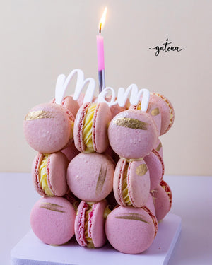 Pink fancy macaroon desserts stacked with gold accents and a lit candle for mom celebration