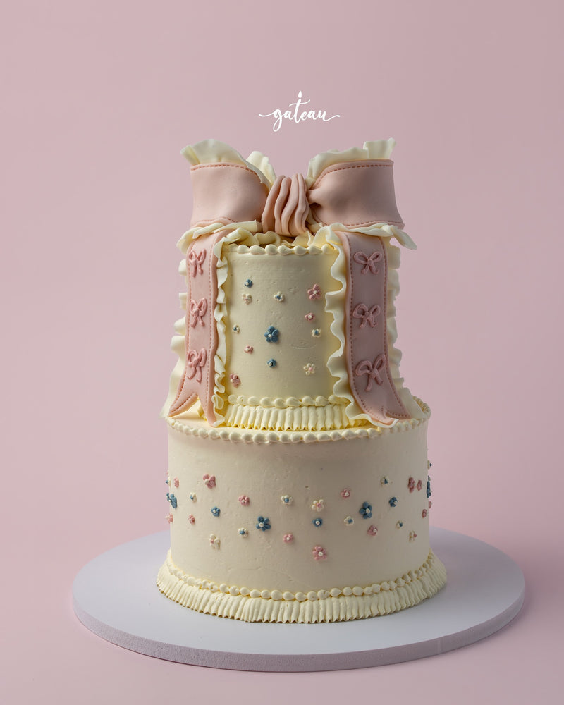 Two-tier delicate Fionka cake with pastel floral decorations and pink ribbon detailing for Fionka cake delivery