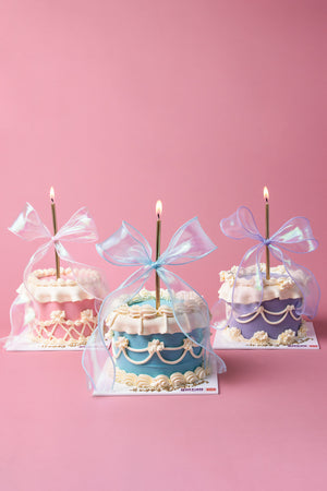 Three Fionka cakes from Gateau Gourmet Cafe decorated with cream and wrapped in sheer blue ribbons with lit candles