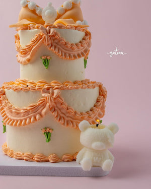 Fionka celebration cake with orange decorative frosting and small floral accents beside a white bear figurine