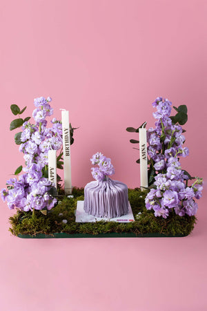 Gateau Gourmet Cafe floral cake arrangement with purple flowers and delicate frosting on a moss base