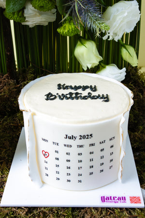 White birthday cake with calendar design for July 2025 by Gateau Gourmet Cafe featuring floral cake designs for summer