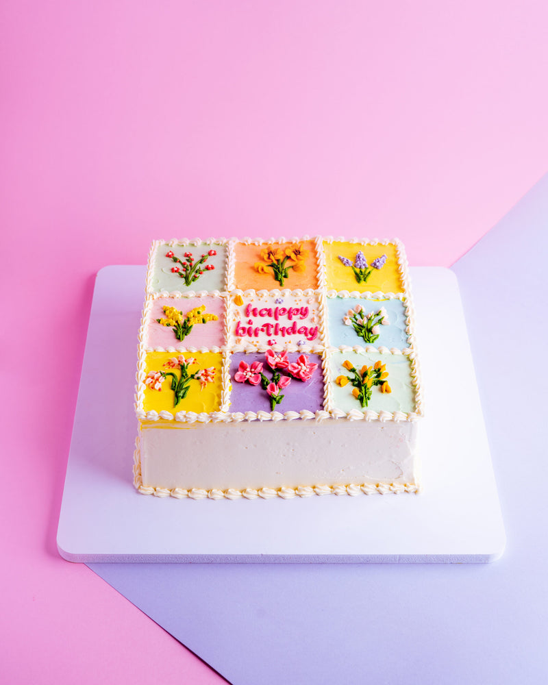 Floral-checkered box cake decorated with colorful flowers and a happy birthday message on top