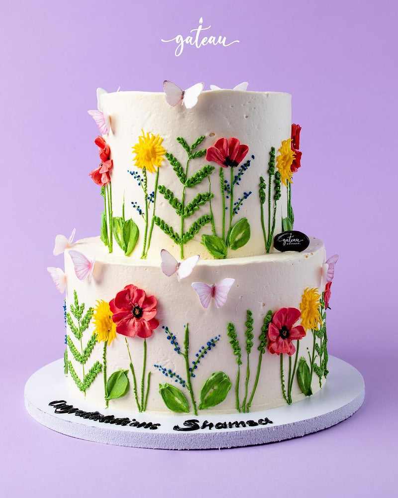 Two-tier flower decorated cake with colorful icing flowers and butterflies from Gateau Gourmet Cafe