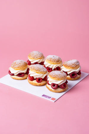 French choux pastry cakes with fresh raspberries and cream from Gateau Gourmet Cafe on a pink background