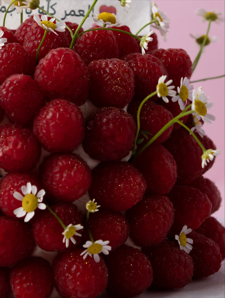 Fresh raspberry cake for delivery topped with vibrant raspberries and delicate flowers