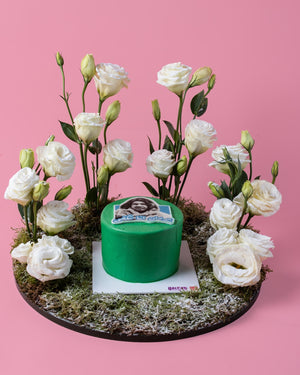 Arabic meme cake by Gateau Gourmet Cafe decorated with white flowers on mossy base against pink background