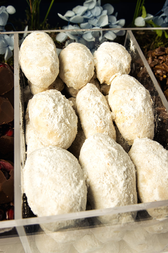 Assorted Arabic sweet treats w arrangement in a clear box, dusted with powdered sugar for a delightful presentation.