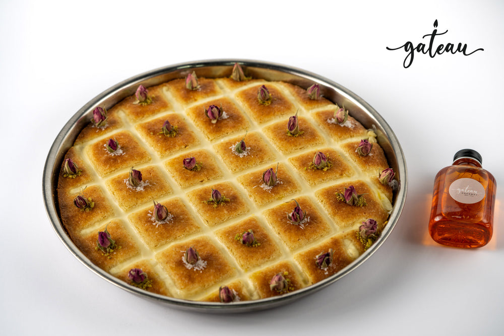 Authentic plain basboosa cake with rosebud toppings in a round metal tray by Gateau Gourmet Cafe