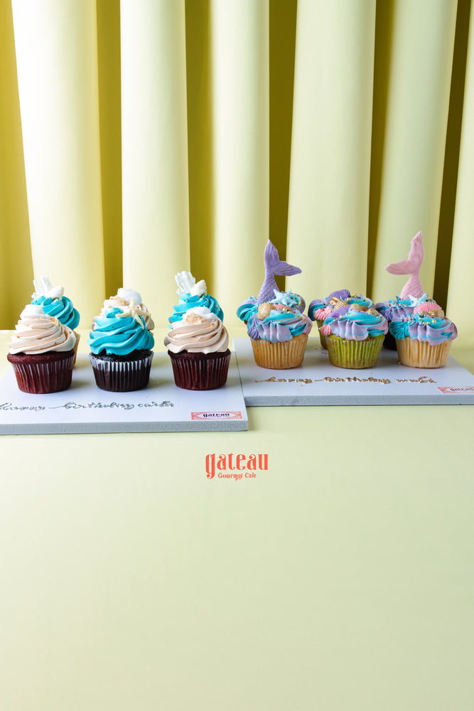 Cupcakes from Gateau Gourmet Cafe featuring beach inspired cupcake flavors with blue and pink frosting and decorative toppers