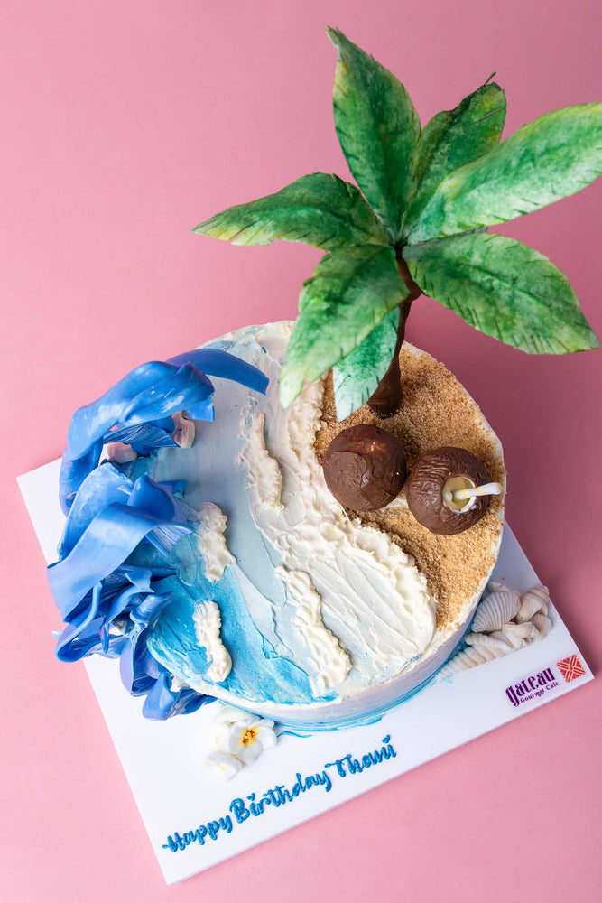 Beach theme cake by Gateau Gourmet Cafe featuring palm tree, blue waves, and sandy shore design