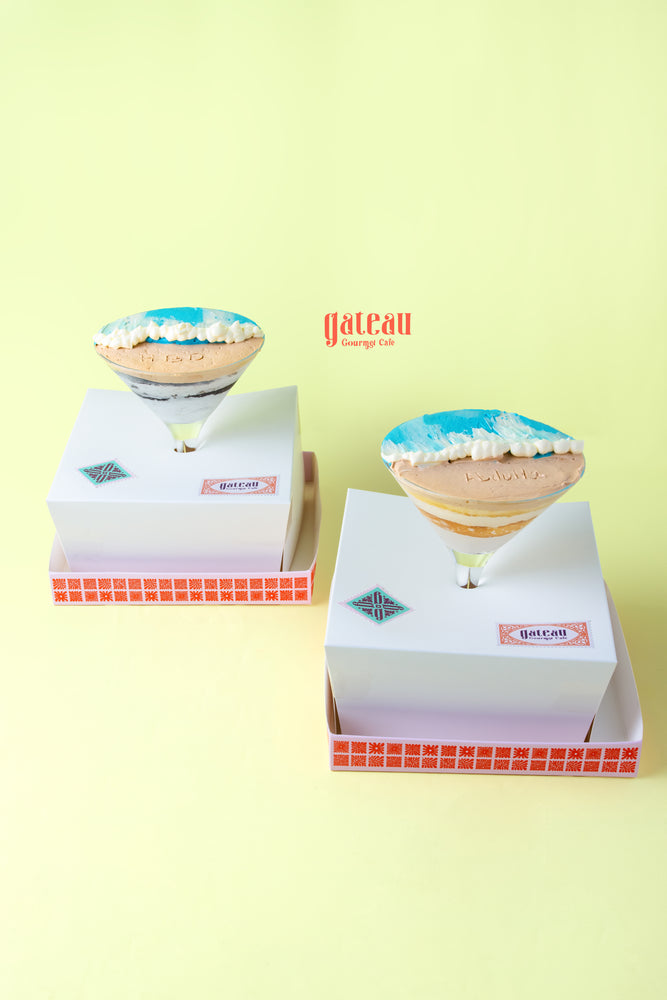 Two beach themed goblet cake desserts in white boxes with colorful icing and tropical designs