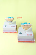 Two beach themed goblet cake desserts in white boxes with colorful icing and tropical designs