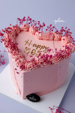 Heart-shaped pink birthday cake with floral decorations available for birthday cake delivery service