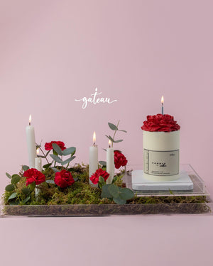 Birthday cake with flower arrangement featuring red roses and white candles on moss by Gateau Gourmet Cafe