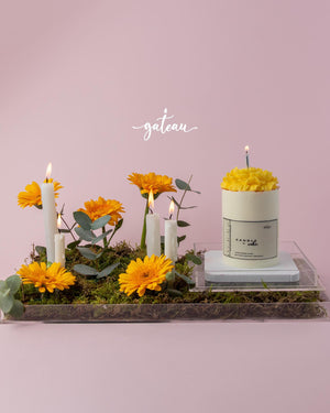 Birthday cake with flower arrangement featuring yellow flowers and candles on a pink background