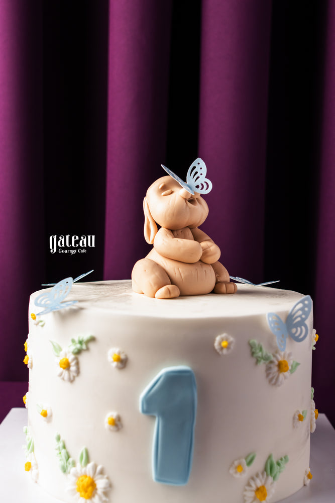 Birthday cake with fondant decorations featuring a sleeping bunny and butterflies from Gateau Gourmet Cafe