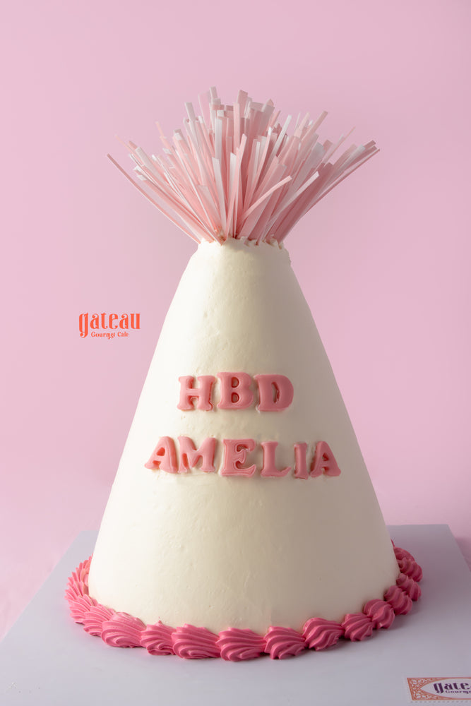 Birthday party hat cake with pink decorations and 'HBD AMELIA' in frosting for festive celebrations